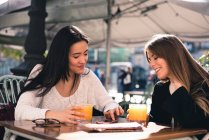 Beautiful friends with a smart phone in the streets of Spain sitting in a cafeteria — Stock Photo