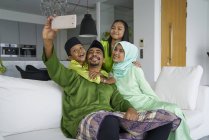 Joven asiático familia celebrando hari raya juntos en casa y tomando selfie - foto de stock