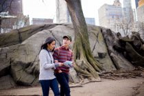 Turistas asiáticos caminando con mapa contra árboles - foto de stock