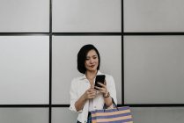 Молодая случайная азиатка, использующая смартфон в торговом центре — стоковое фото