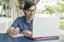 Estudiante malayo trabajando en el proyecto escolar en el ordenador portátil - foto de stock