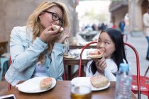 Felice giovane madre con sua figlia mangiare insieme in un caffè — Foto stock