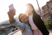 Feliz joven madre con su hija tomando una selfie con su teléfono de la cámara - foto de stock