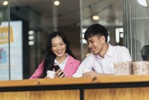 Attractive young asian couple drinking coffee and using smartphone — Stock Photo