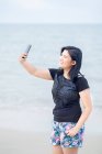 Adolescent avec téléphone intelligent prenant selfie par la plage. — Photo de stock