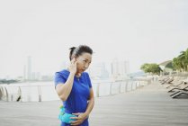Young sporty asian woman with earphones at pier — Stock Photo