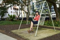 Молода леді, використовуючи її мобільний телефон в парку, Сінгапур — стокове фото