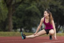 Una giovane donna asiatica si sta allungando su una pista in caso di maltempo. Si sta preparando per l'esercizio quotidiano, nonostante il tempo
. — Foto stock
