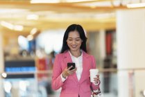 Молода приваблива азіатська жінка використовує смартфон у торговому центрі — стокове фото
