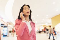 Junge attraktive asiatische Frau mit Smartphone in Einkaufszentrum — Stockfoto