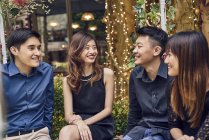 Compañía de jóvenes asiáticos amigos juntos sentado en banco al aire libre - foto de stock
