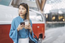 Atractivo joven asiático chica usando smartphone y café taza - foto de stock
