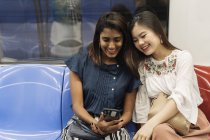 Jóvenes casual asiático niñas compartir smartphone en tren - foto de stock