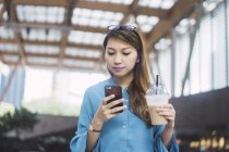 Привлекательная молодая азиатская девушка с помощью смартфона и кофейной чашки — стоковое фото