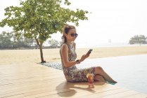 Joven hermosa mujer asiática usando smartphone por piscina - foto de stock