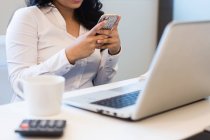 Cropped image of young woman using smartphone in modern office — Stock Photo