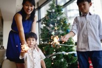Familia asiática celebrando vacaciones de Navidad con chispas de fuegos artificiales - foto de stock