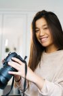 Jeune femme chinoise regardant la caméra souriant et tenant une caméra — Photo de stock