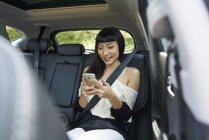 Молода жінка на задньому сидінні автомобіля за допомогою мобільного телефону — стокове фото