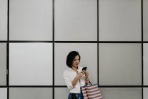 Giovane donna asiatica casuale utilizzando intelligente al centro commerciale — Foto stock