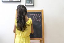 Вид ззаду молодої дівчини, що пише на крейдовій дошці — стокове фото