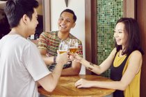 Young asian friends cheering beer together in bar — Stock Photo