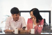 Attractive young asian couple sharing coffee and smartphone — Stock Photo