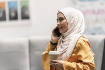 Jeune femme d'affaires asiatique en hijab en utilisant un smartphone dans un bureau moderne — Photo de stock