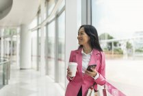 Atractivo joven asiático mujer beber café y el uso de teléfono inteligente - foto de stock