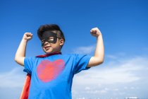 Superhéros enfant fléchissant ses muscles contre le ciel bleu — Photo de stock