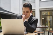 Joven asiático exitoso hombre de negocios usando laptop - foto de stock