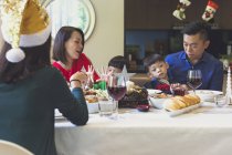 Family of four enjoys a festive dinner with a friend during Christmas holidays. — Stock Photo