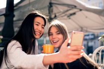 Dos hermosas mujeres tomando selfie en un café - foto de stock