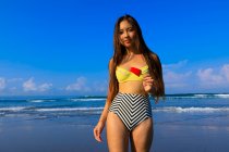Ragazza asiatica su una spiaggia in bikini con un gelato in mano . — Foto stock