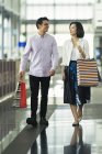 Joven casual asiático pareja con bolsas en compras en mall - foto de stock