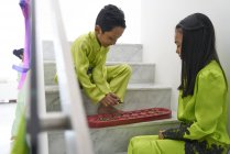 Маленькие азиатские дети празднуют Хари Райя вместе дома и играют в игру на ступеньках — стоковое фото