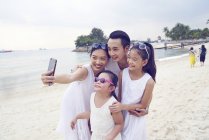 Feliz asiático familia pasando tiempo juntos en playa y tomando selfie - foto de stock