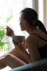 Chinese young woman having breakfast on the sofa at home — Stock Photo