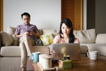 Madura asiática casual pareja usando digital dispositivos en casa - foto de stock