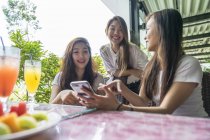 Three asian girls looking at the smartphone together in cafe — Stock Photo