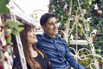 Couple of young asian friends together sitting near fir tree — Stock Photo