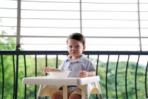 Хлопчик їсть у дитячому кріслі на балконі — стокове фото