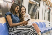 Young casual asian girls sharing smartphone it train — Stock Photo