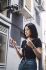 Молодая красивая азиатская девушка в повседневной одежде с помощью смартфона на улицах города — стоковое фото