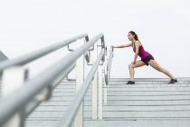 Una joven asiática se estira en una escalera afuera antes de correr . - foto de stock