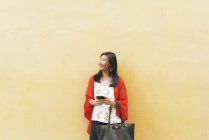 Jovem asiático mulher posando contra amarelo parede com smartphone — Fotografia de Stock