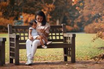 Bonito asiático mãe e filha usando smartphone no banco no parque — Fotografia de Stock