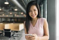 Jovem asiático bem sucedido mulher de negócios com smartphone no escritório moderno — Fotografia de Stock
