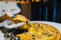 Abgeschnittenes Bild einer Frau, die in gemütlicher Bar ein Stück Pizza einnimmt — Stockfoto