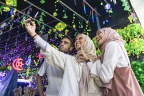 Young group of muslim friends taking selfie against the hari raya decorations. — Stock Photo